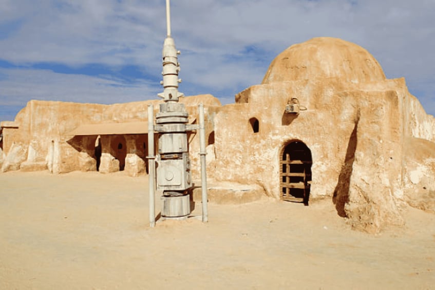 A desert landscape with a large, beige dome-shaped building and a tall, slender minaret. 1