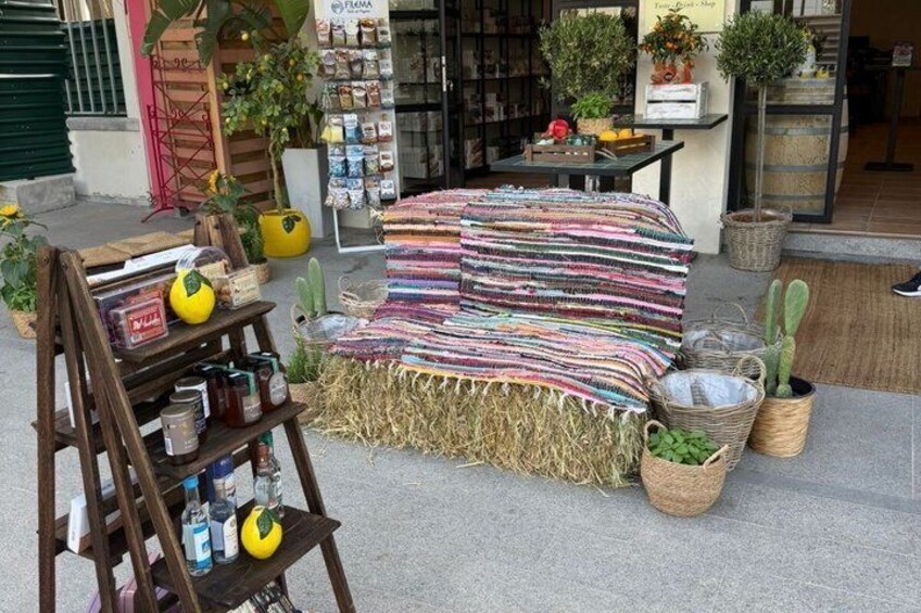 A storefront with a striped blanket, plants, and a wooden shelf with jars. 2