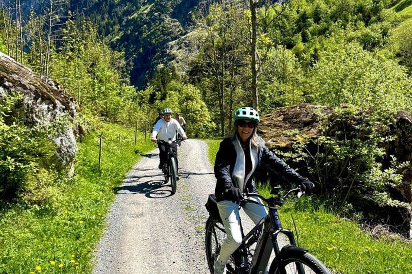 Two cyclists on a gravel path surrounded by greenery and hills. 2