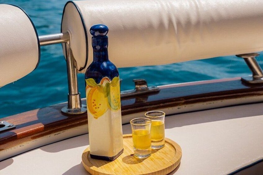 A bottle of liquor and two shot glasses on a wooden tray on a boat. 1