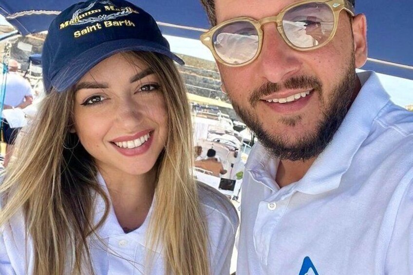 Two people wearing casual clothing, one with a cap and the other in a polo shirt, outdoors with boats in the background. 2