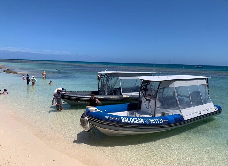 Two boats on a beach with clear water and people in the background. 2