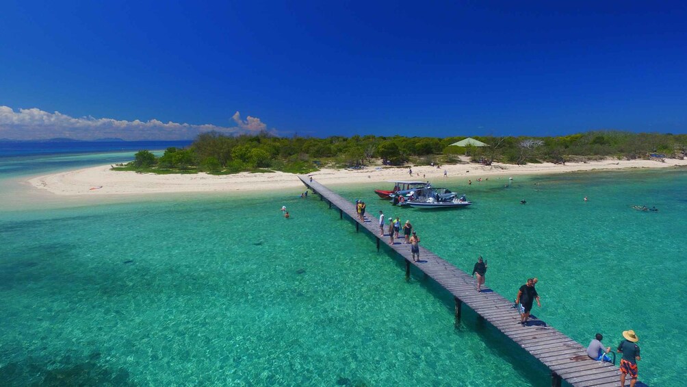 A wooden pier extending into clear turquoise waters, surrounded by a sandy beach and lush greenery. 1