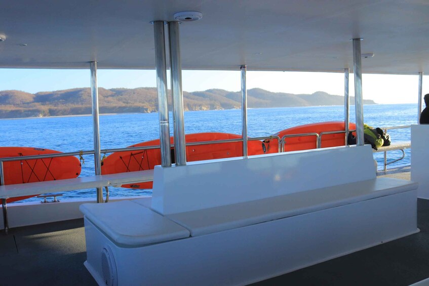 A boat interior with a bench, orange life jackets, and a view of the water and hills. 2