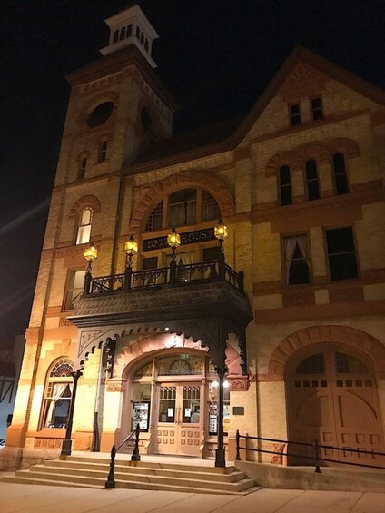 A historic building with a tower, arched windows, and a balcony with lights. 1
