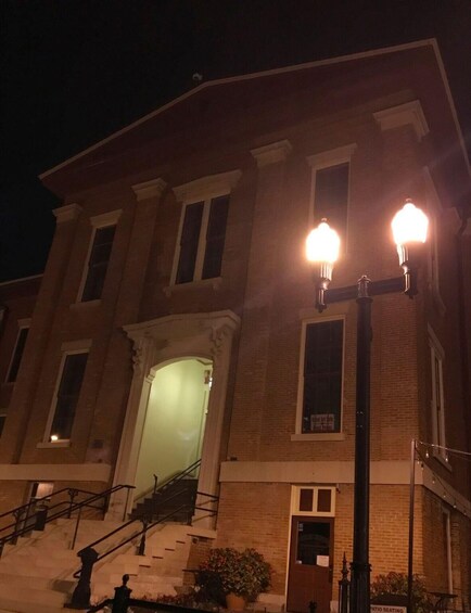 A brick building with a staircase, a lit street lamp, and a sign for patio seating. 2