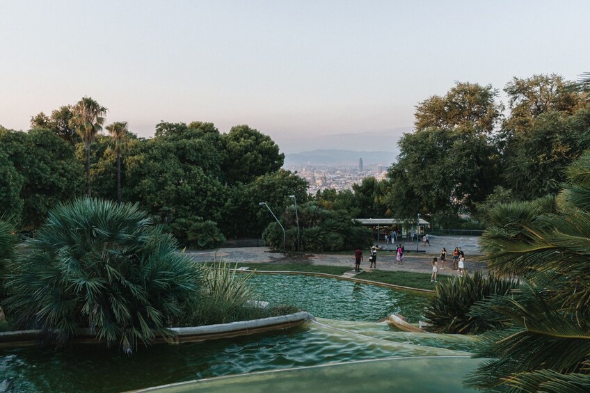 A park with a water feature, trees, and a distant cityscape. 2