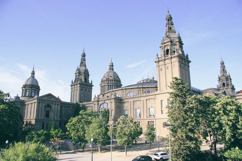 A large historic building with multiple domes and towers, surrounded by trees and a clear sky. 1