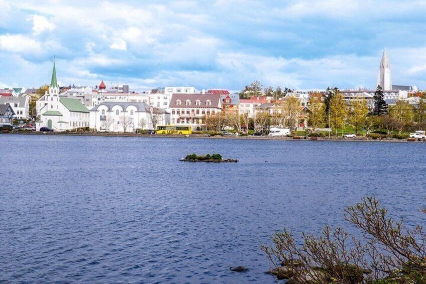 A calm lake with a small island, a church with a green roof, and a tall tower in the background. 5