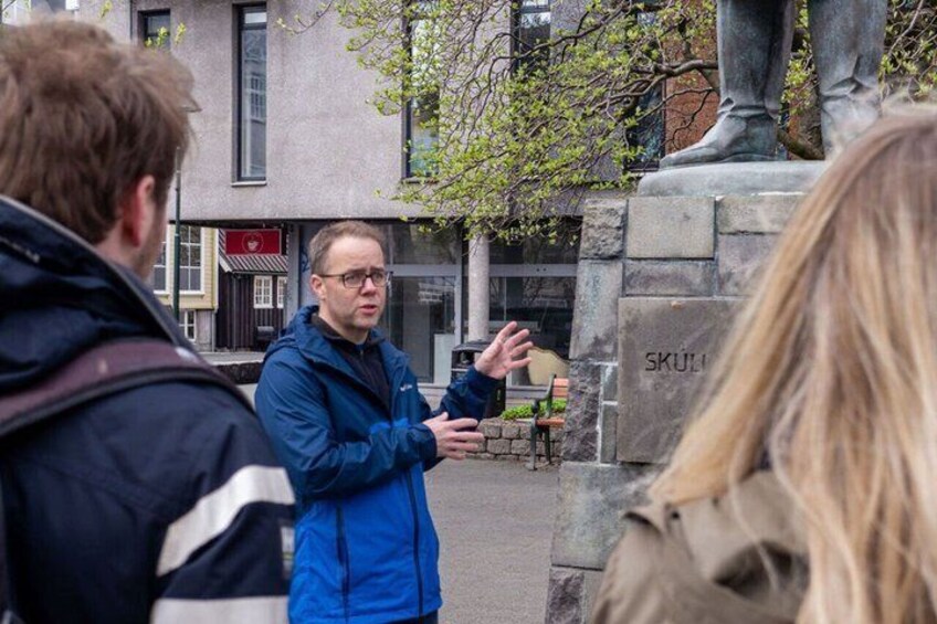 A person gesturing in an urban setting with a statue and buildings in the background. 1