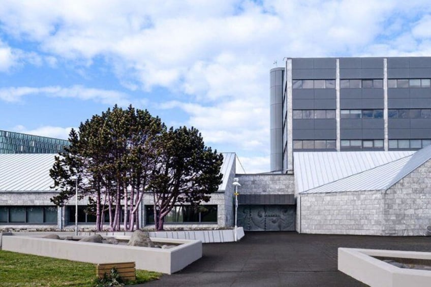 A modern building with a glass facade, a tree-lined courtyard, and a clear sky. 3