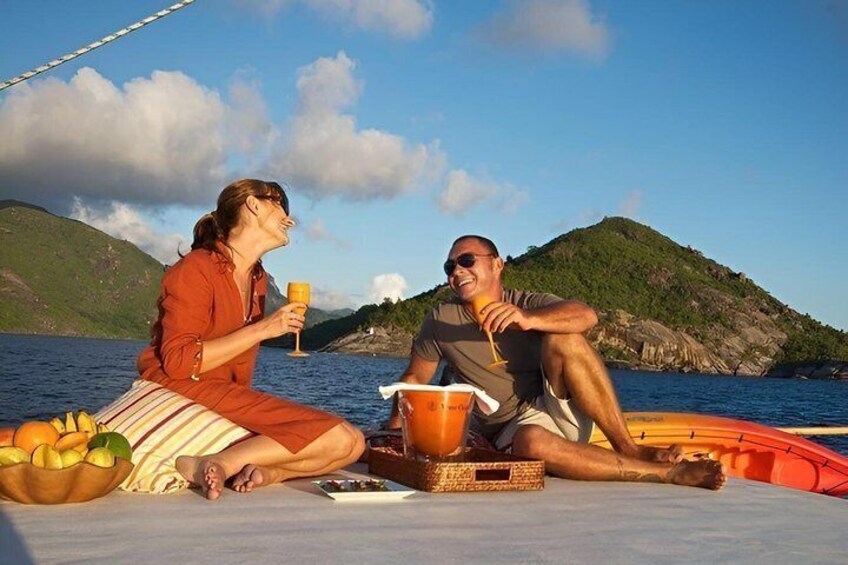Two people sitting on a boat with a basket of fruit and a bottle of wine. 5