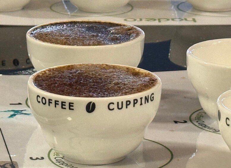 Two white ceramic cups with 'COFFEE CUPPING' text, placed on a tray with similar cups. 1