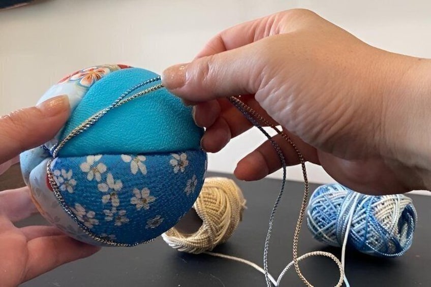 Hands holding a crocheted ball with floral patterns, yarn, and a crochet hook. 4
