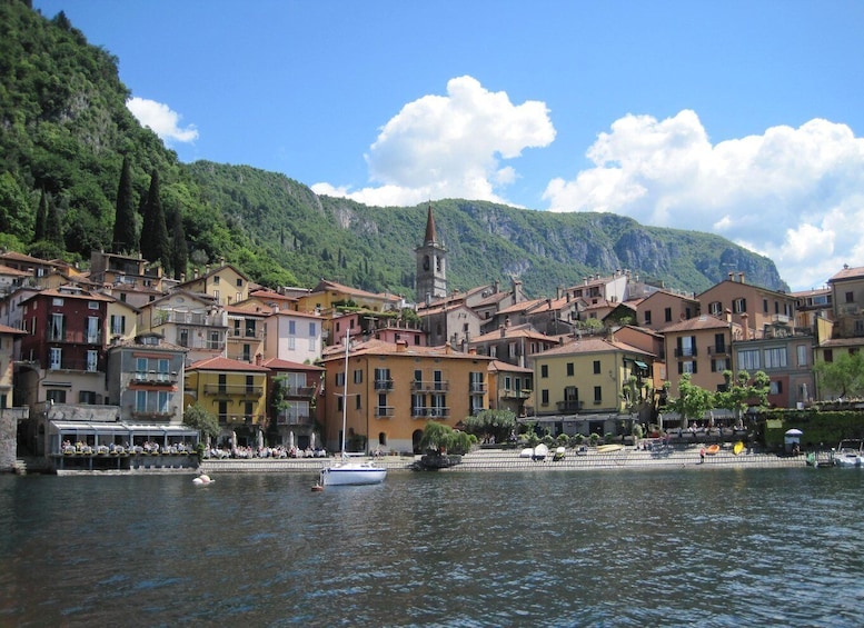 A lakeside town with colorful buildings, a church steeple, and a boat on the water. 2