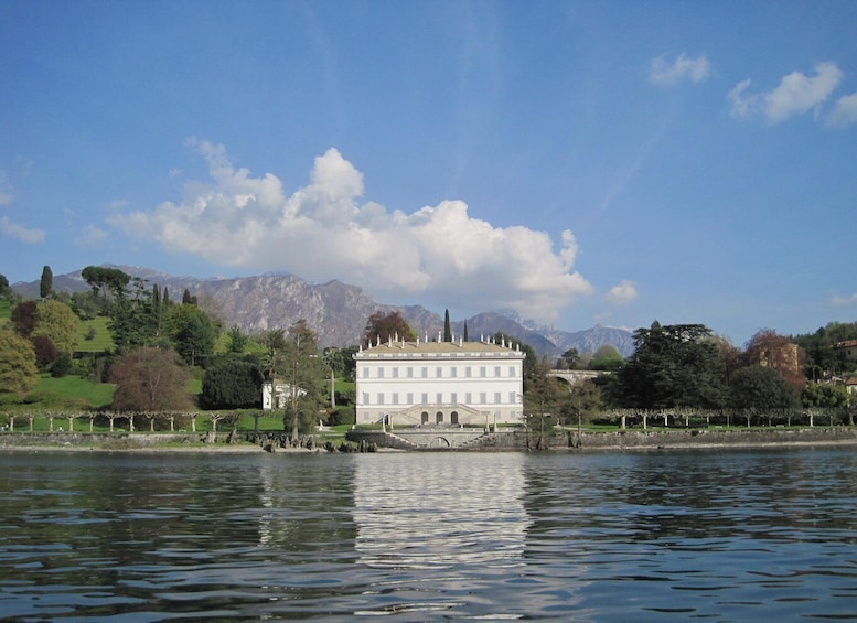 A large white building by a calm lake with mountains in the background. 3