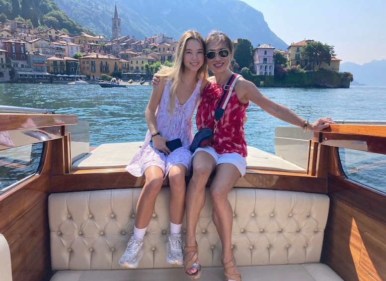 Two people on a boat with a coastal town and mountains in the background. 1