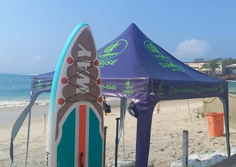 A beach with a surfboard, a purple tent, and the ocean in the background. 3
