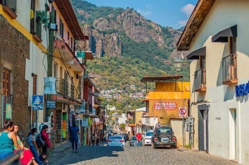 A cobblestone street lined with buildings, a mountain in the background, and a sign for 'PISADA.' 3