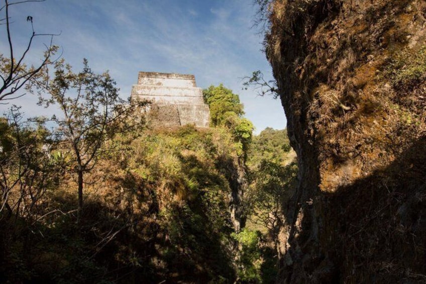A stone structure atop a hill, surrounded by dense forest. 1