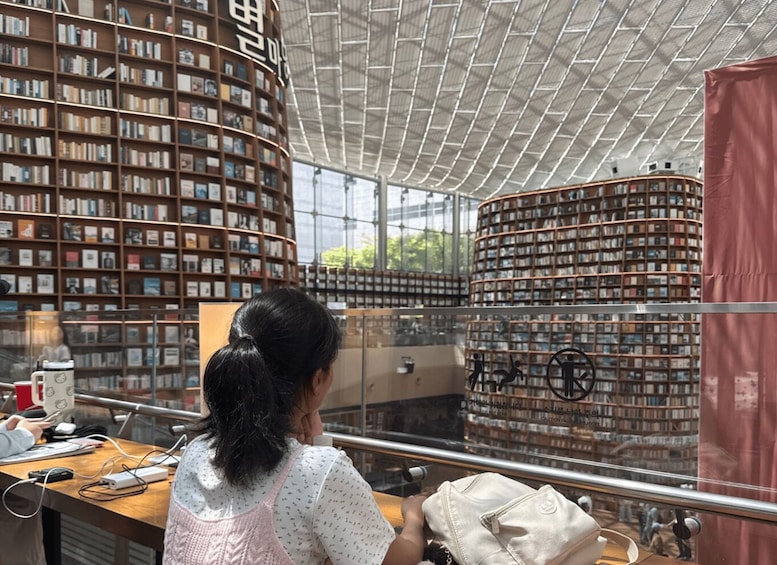 A person reading at a table in a library with large bookshelves and a glass railing. 2