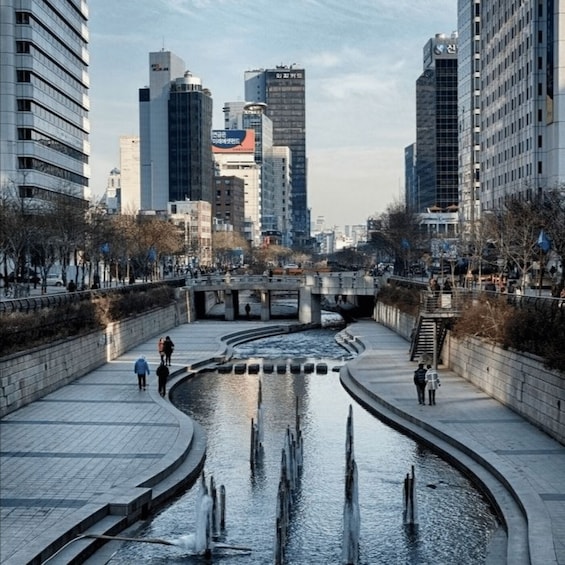 A cityscape with a curved water feature, modern buildings, and people walking along the paths. 5