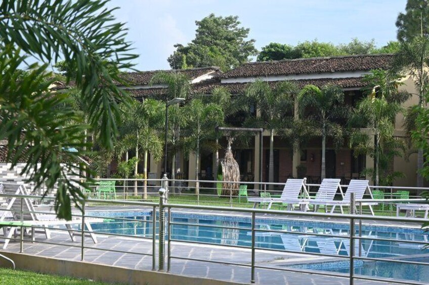 A swimming pool with lounge chairs, a tiled deck, and a building with a tiled roof in the background. 2