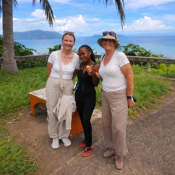Three people standing by a bench with a coastal view in the background. 2