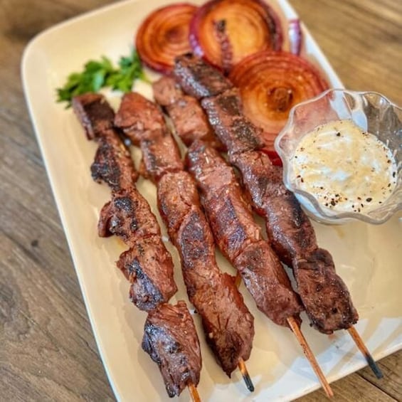 Skewered meat on a plate with sliced onions and a side of sauce. 3