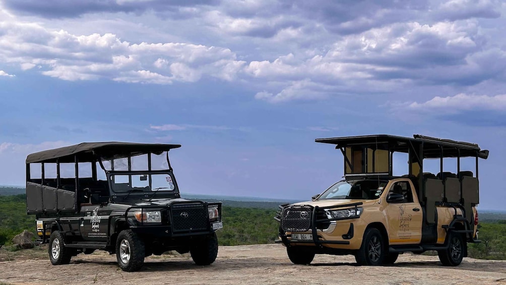 Two safari vehicles parked on a dirt road with a cloudy sky above. 1
