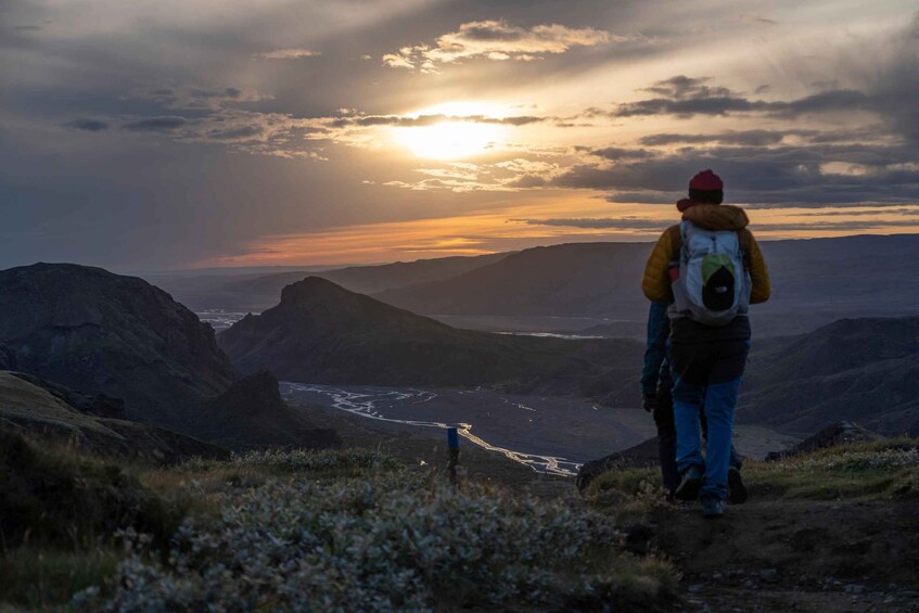 A hiker on a mountain trail with a river below, under a sunset sky. 3