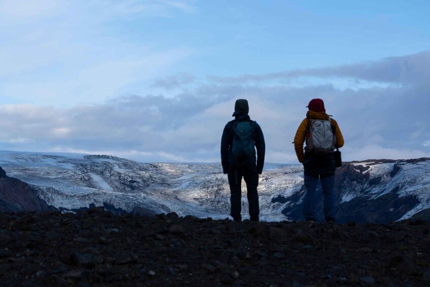 Two hikers on a rocky terrain with a glacier in the background. 4
