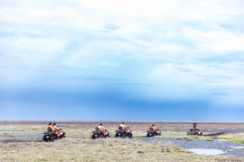 Four people on all-terrain vehicles in a flat, open landscape with a cloudy sky. 3