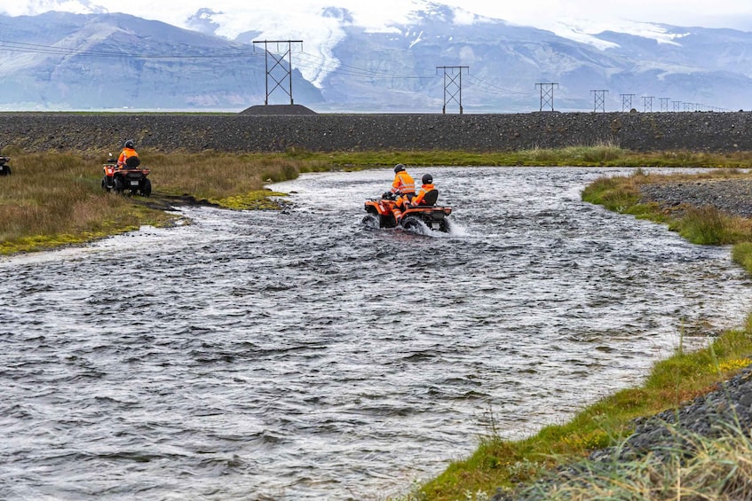 Two people on an ATV crossing a river in a rugged landscape with mountains in the background. 5