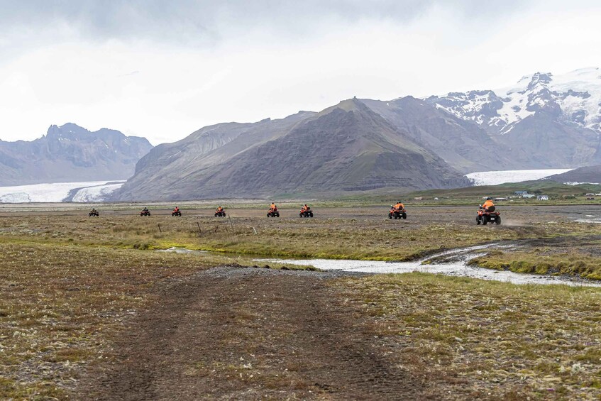 A group of people on ATVs in a rugged landscape with a glacier and mountains in the background. 2