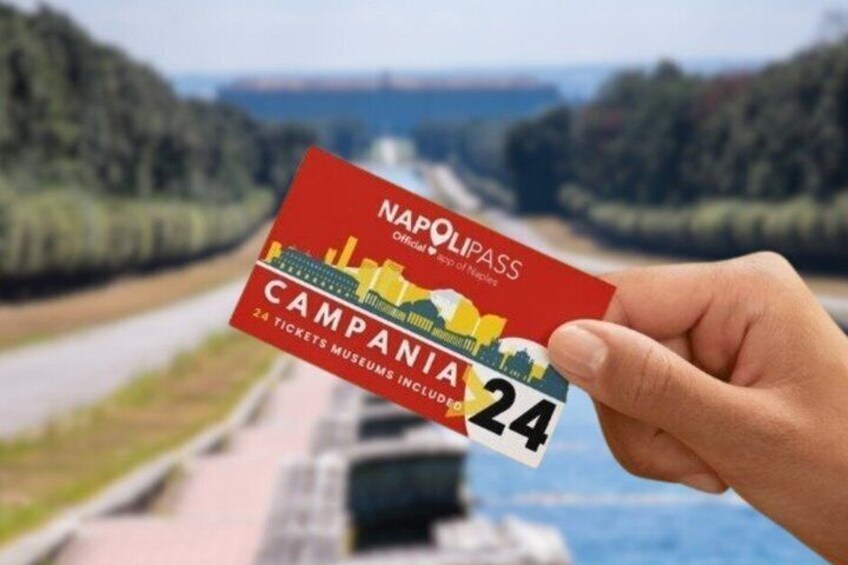 A hand holding a red and yellow ticket for the Campania region, with a scenic view of a road and greenery in the background. 1