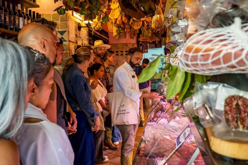 A group of people in a market with hanging vegetables and packaged meat. 2