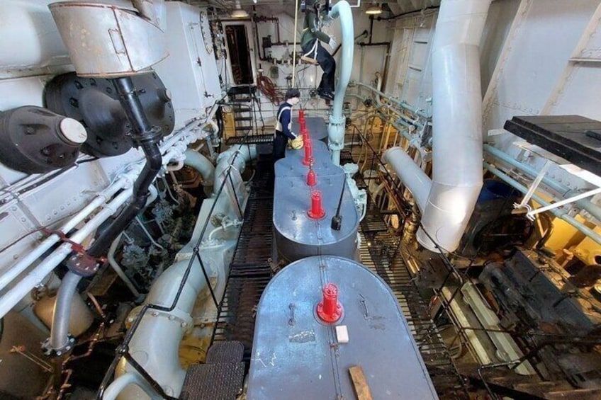 A ship's engine room with visible pipes, machinery, and a worker in uniform. 2