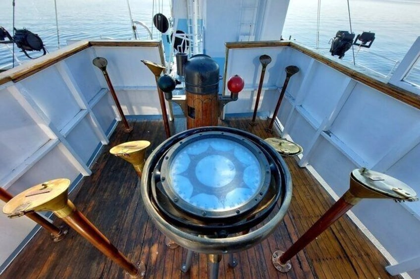 A ship's deck with a central circular window, wooden railings, and a compass. 5