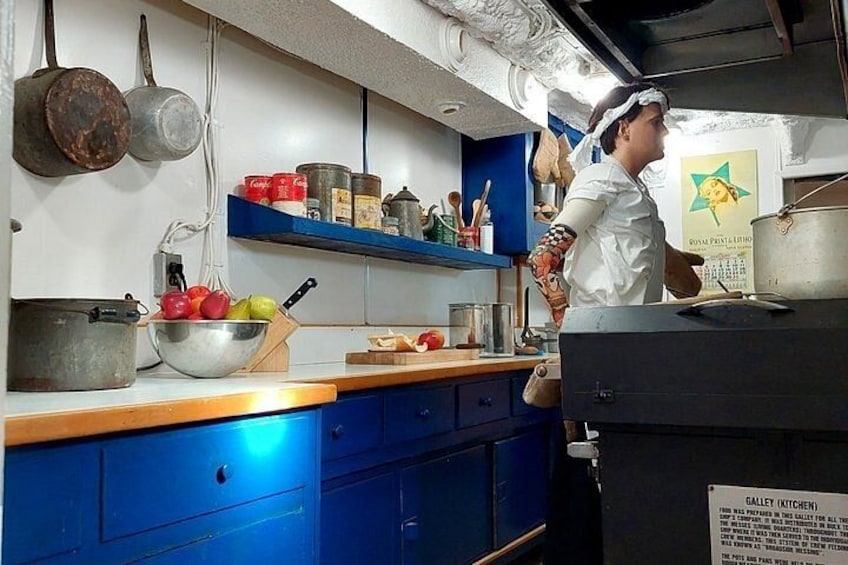A kitchen with blue cabinets, a metal bowl of fruit, and a person cooking. 3