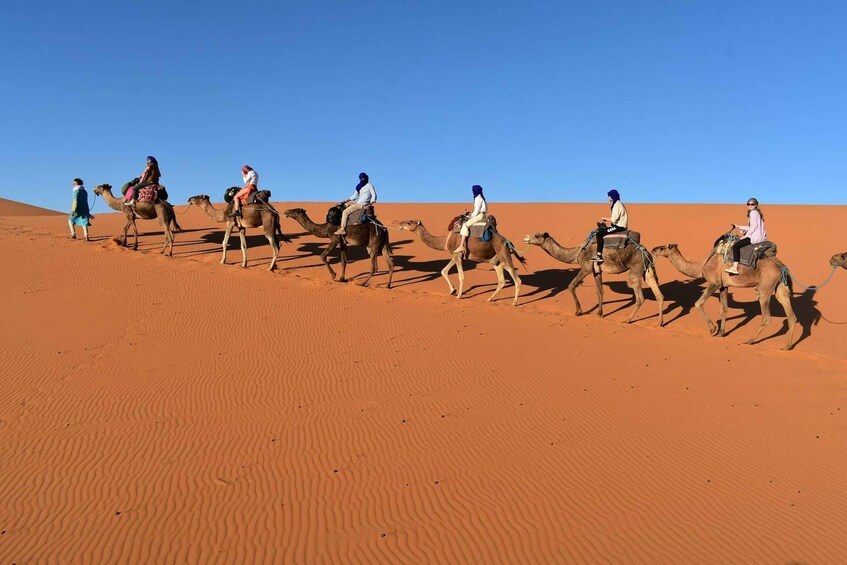 A group of people riding camels across a desert landscape with sand dunes. 4