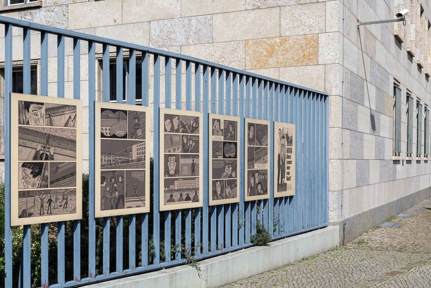 A blue metal fence with black-and-white photographs depicting various scenes. 5