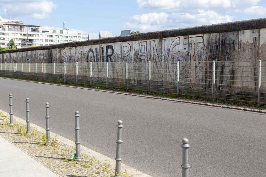 A road with a fence and bollards, a wall with graffiti, and buildings in the background. 4