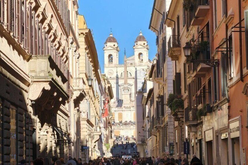 A historic street with ornate buildings, a prominent church with two towers, and a crowd gathered at the church's entrance. 3