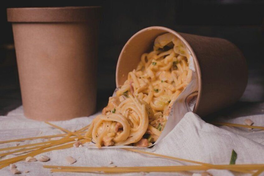 A cup of pasta with a wooden spoon, pasta on a cloth, and a brown paper cup. 4