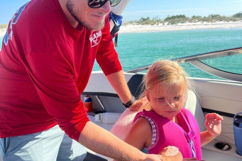 A man in a red shirt and a child in a pink life jacket on a boat. 2