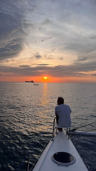 A person sitting on a boat's deck, facing the ocean during sunset. 5