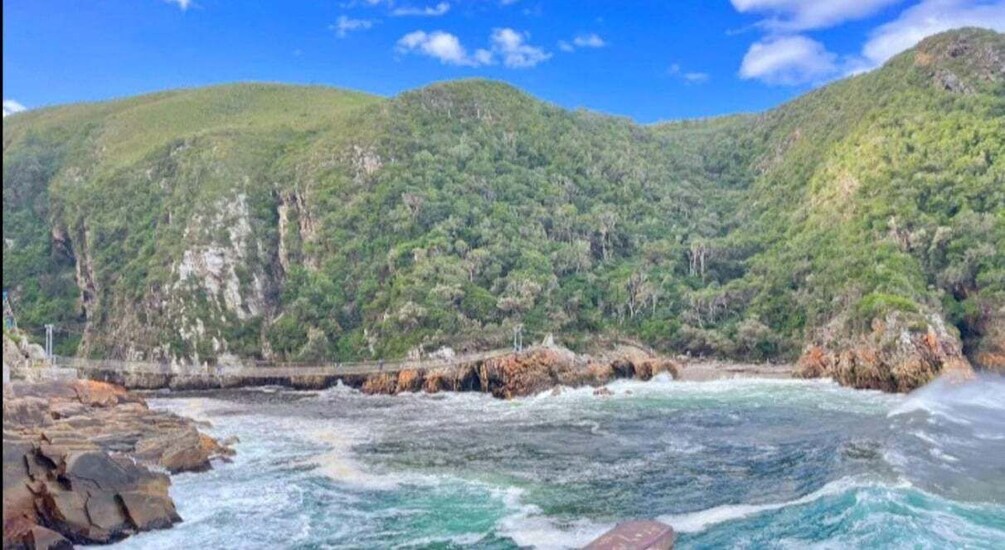A coastal landscape with rocky shores, waves, and lush green hills. 5