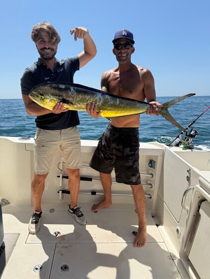 Two people on a boat holding a large fish. 1