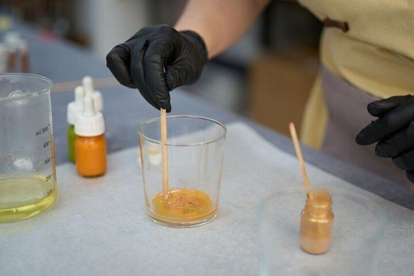 A person wearing black gloves handling a glass container with a yellow liquid and a wooden stick. 5